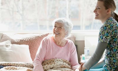 Smiling elderly woman and caregiver in a room.