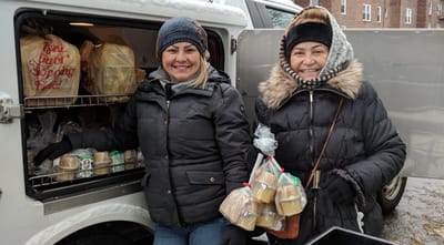 Two women with food packages smiling outdoors.