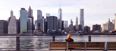 Person sitting on a bench overlooking a skyline.