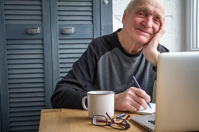 Cheerful elderly man writing at a table