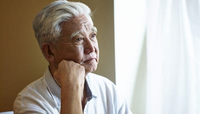 An elderly man deep in thought indoors.