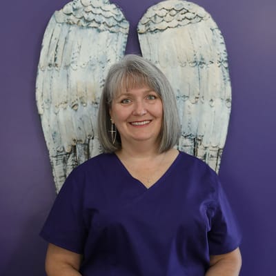 Staff member in purple scrubs with angel wings backdrop.
