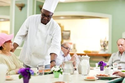 A chef serving food to residents in the dining area