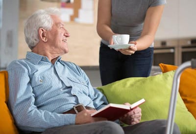 Resident enjoying coffee with staff in a cozy setting.