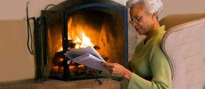Senior reading by a cozy fireplace indoors.
