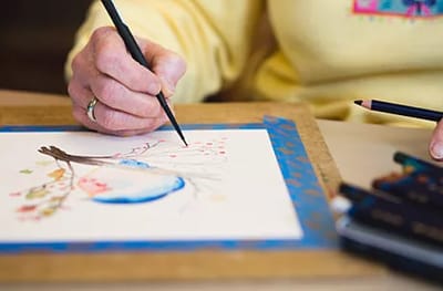 An elderly person's hand painting a colorful drawing.