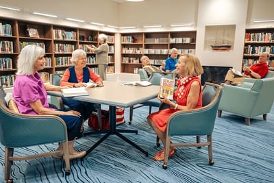 Residents engaged in reading and conversation in a library area.