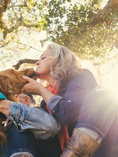 Woman kissing a dog outdoors, sunny setting.