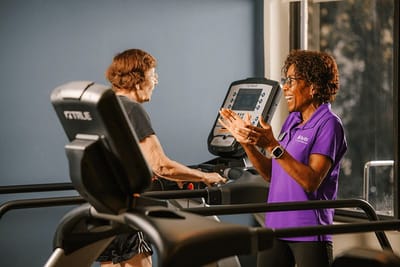 Resident exercising on treadmill with staff encouragement.