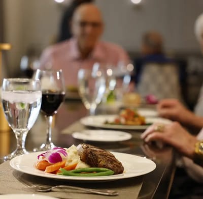 Residents enjoying a meal with steak and vegetables.