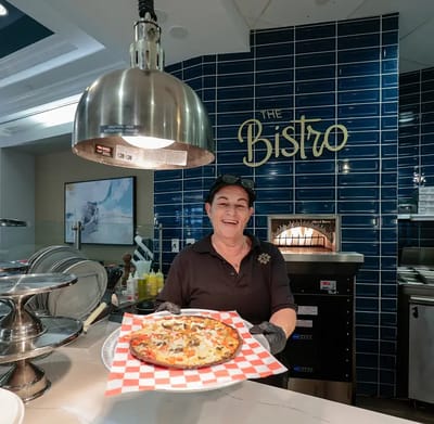 Staff member presenting a fresh pizza in the dining area.