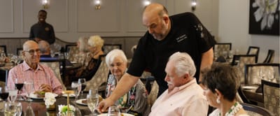 Residents dining with a chef in a shared space.