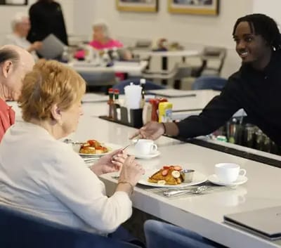 Staff serving food to residents in the dining area.