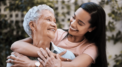 Senior resident and caregiver smiling together outdoors.
