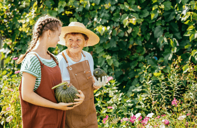 Senior woman and girl holding pumpkins in garden