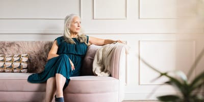 Senior woman sitting thoughtfully on a pink sofa.