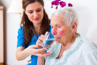 Caregiver assisting an elderly woman with a drink