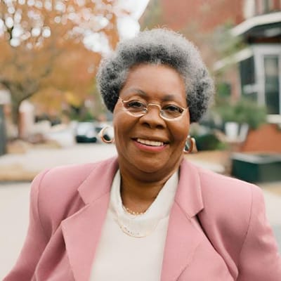 A smiling senior woman in a pink jacket outdoors