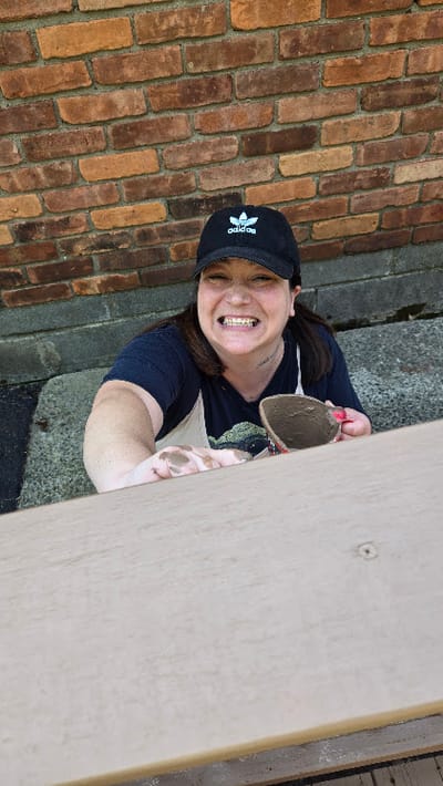 Person outdoors smiling while reaching for a pot.