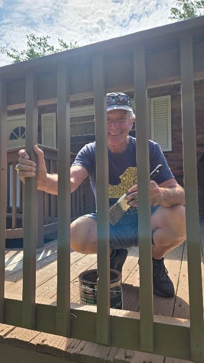 A man painting a wooden railing outdoors.