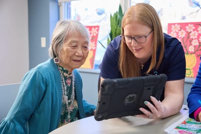 Staff assisting a resident with a tablet in a common area.