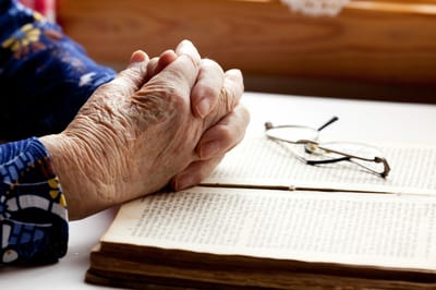 Elderly hands resting on an open book with glasses nearby