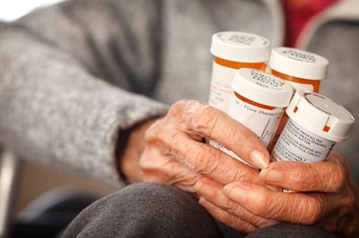 Hands holding multiple prescription medication bottles.