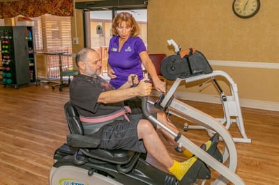 Staff assisting a resident with exercise equipment.