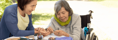 Resident and staff engaged in a craft activity outdoors.