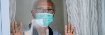 Elderly man wearing a mask, looking through a window.