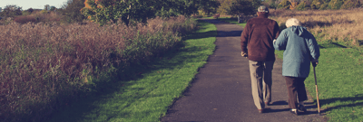 Two seniors walking on a path in a park.