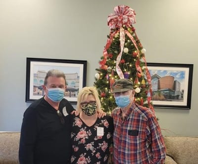 Residents and staff smiling by a holiday tree.