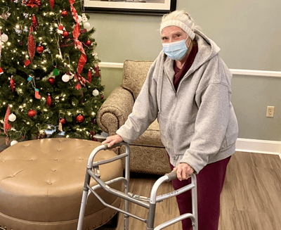 Resident using a walker near a Christmas tree.
