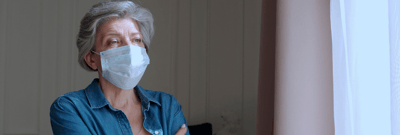 Senior woman in a mask looking out of a window.
