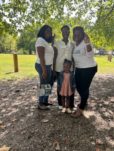 Four individuals posing outdoors in a park.
