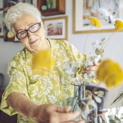 Senior woman arranging flowers indoors.