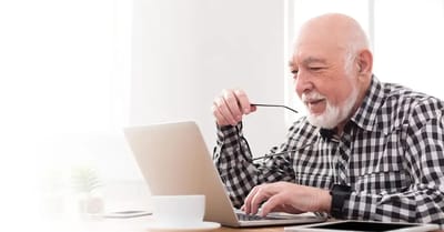 An elderly man using a laptop at a table