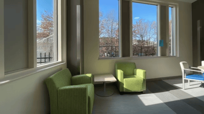 Bright lounge area with green chairs and large windows.