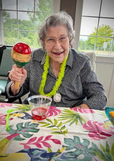 A smiling senior woman holding a maraca at a table