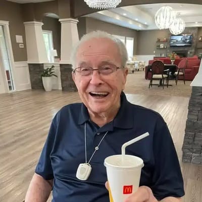 A smiling elderly resident with a drink in a common area