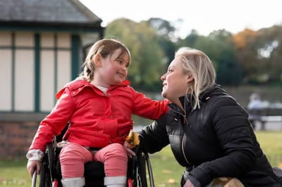 A woman interacting with a young girl in a wheelchair outdoors