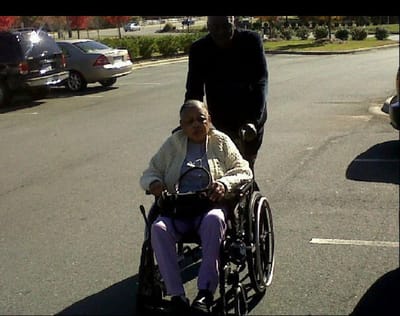 A resident in a wheelchair being pushed outside by a caregiver