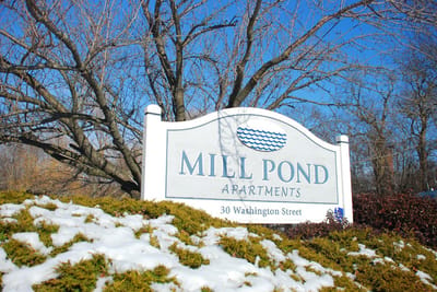 Sign for Mill Pond Apartments next to a snowy garden