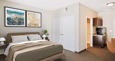 A cozy resident room with a bed, art, and kitchenette