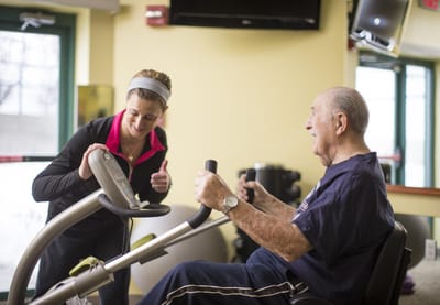 Senior man exercising with staff assistance in a fitness area