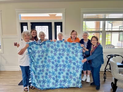 Residents and staff holding a handmade quilt in the common area