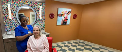 A caregiver styling a resident's hair in a vibrant interior space
