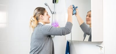 Staff member cleaning a mirror in a bathroom