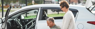 A caregiver assisting a senior getting into a vehicle.