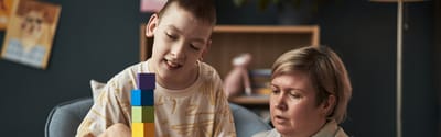 Child and caregiver playing with colorful building blocks.